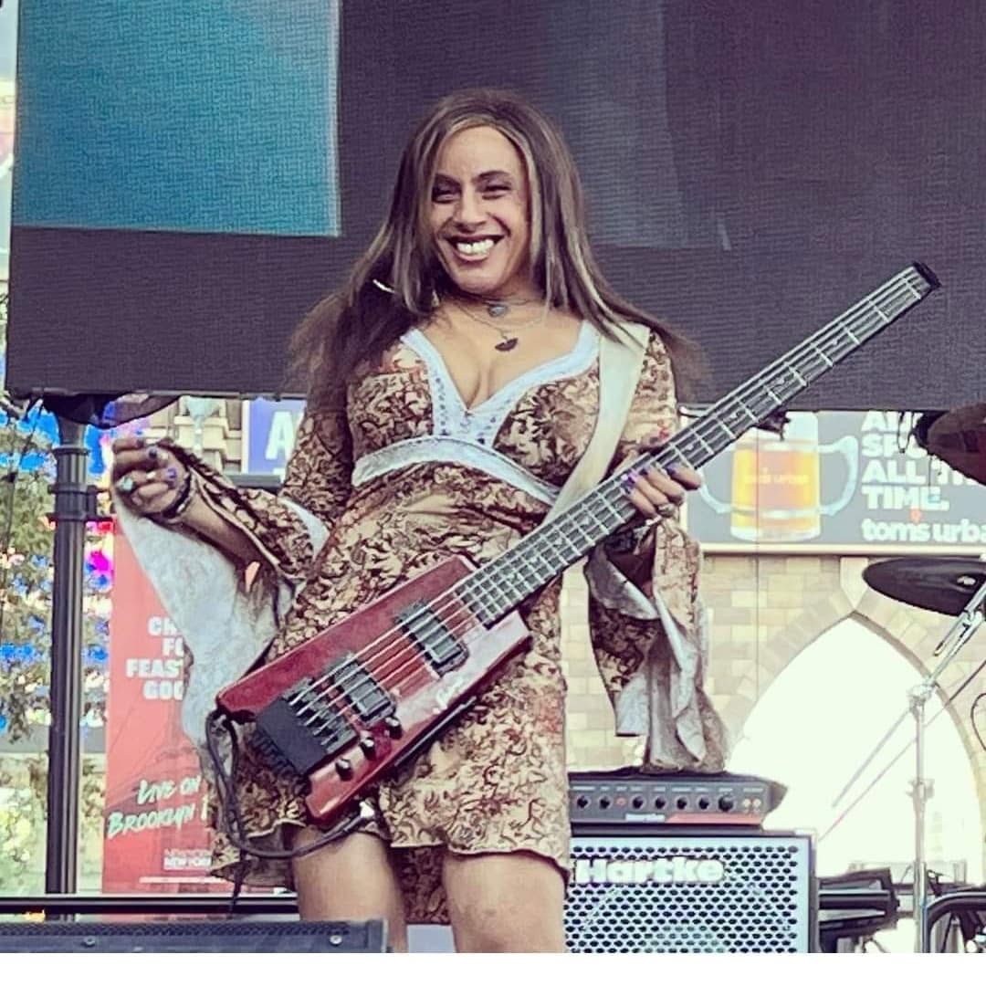 Merry Adin smiling with her bass during an outdoor performance