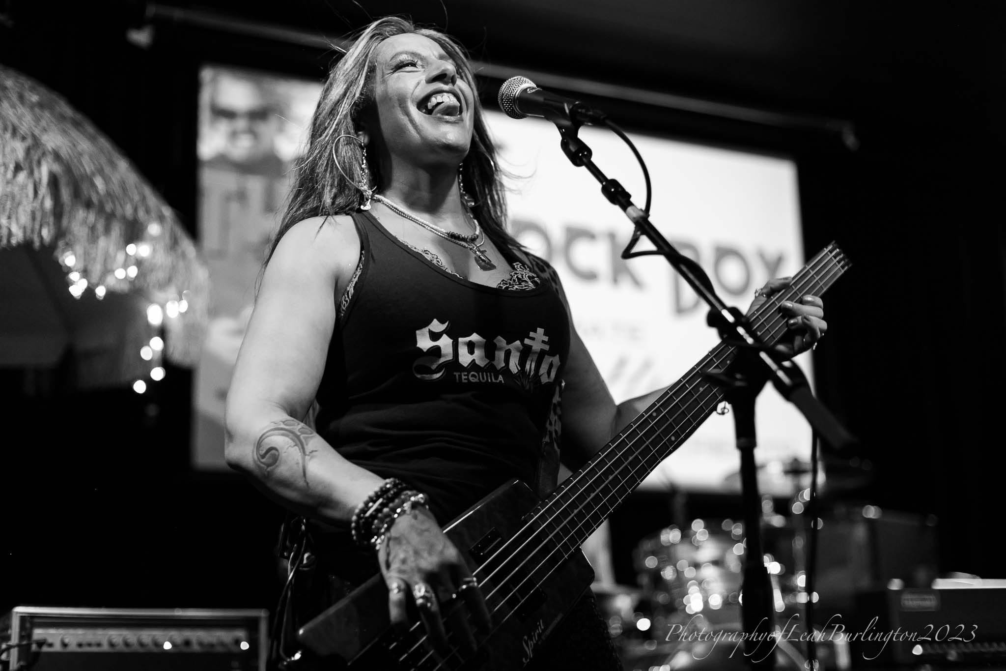 Merry Adin singing and playing bass in a black-and-white live photograph