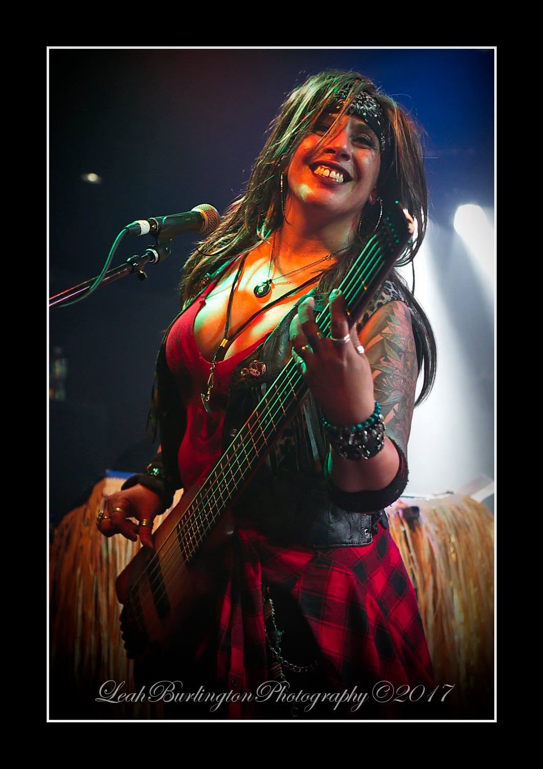 Merry Adin smiling toward the audience while singing and playing bass