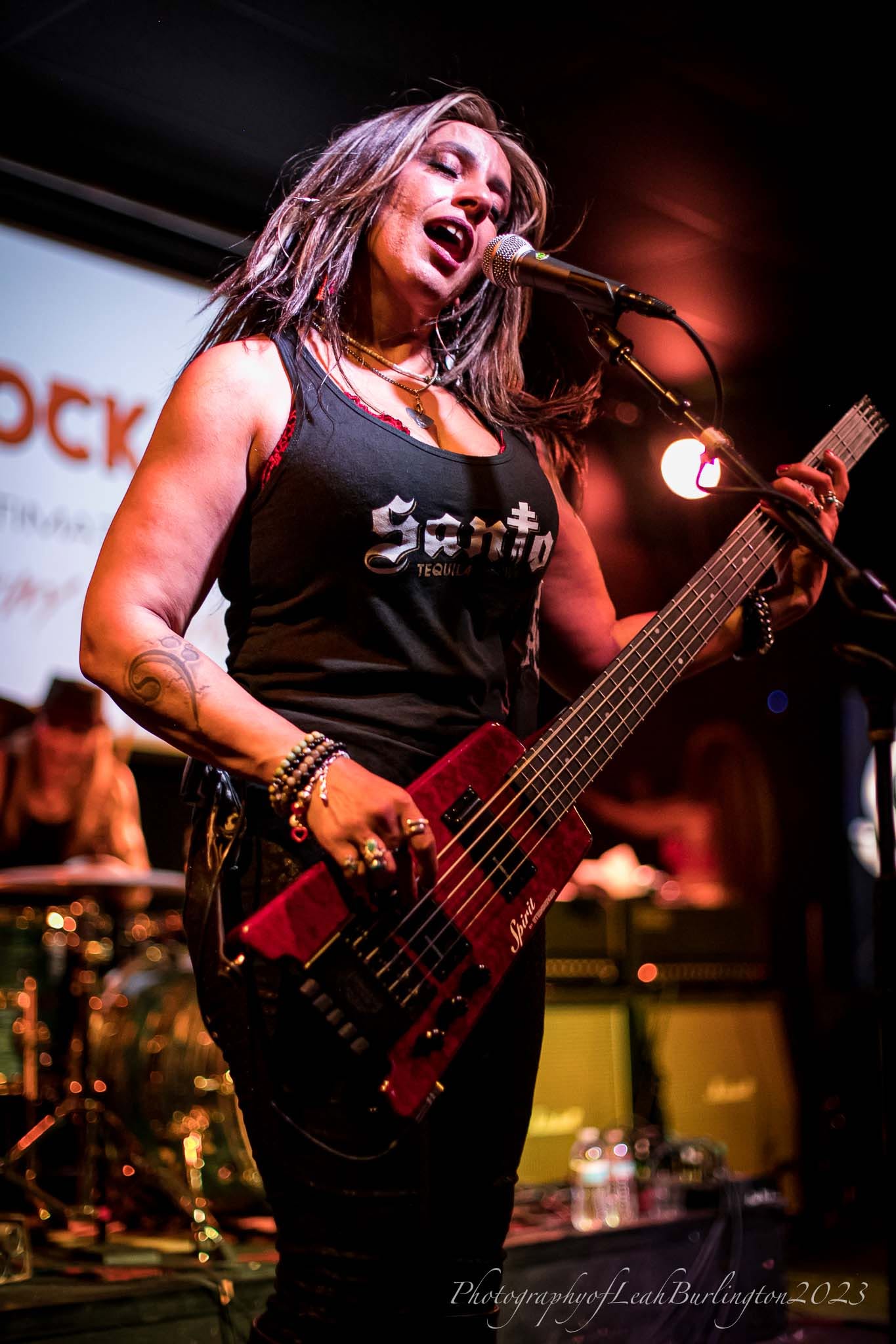 Merry Adin singing and playing her red bass under warm stage lights